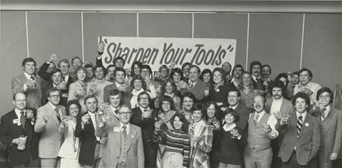 Black and white photo of a group of people - Sign Says "Sharpen Your Tools"